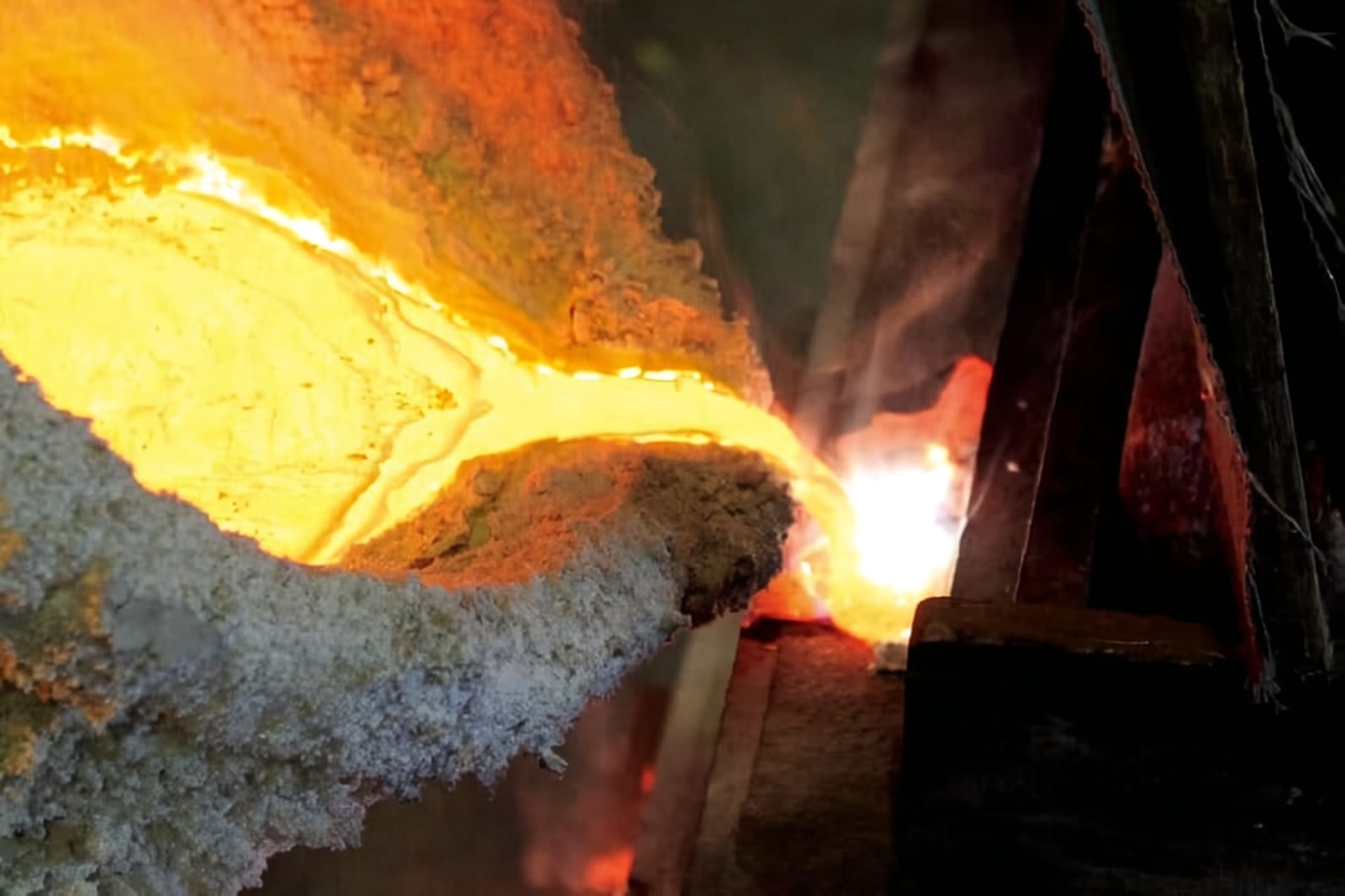 Molten metal being poured from a crucible in the Nousaku foundry in Takaoka, glowing amber against the dark workshop