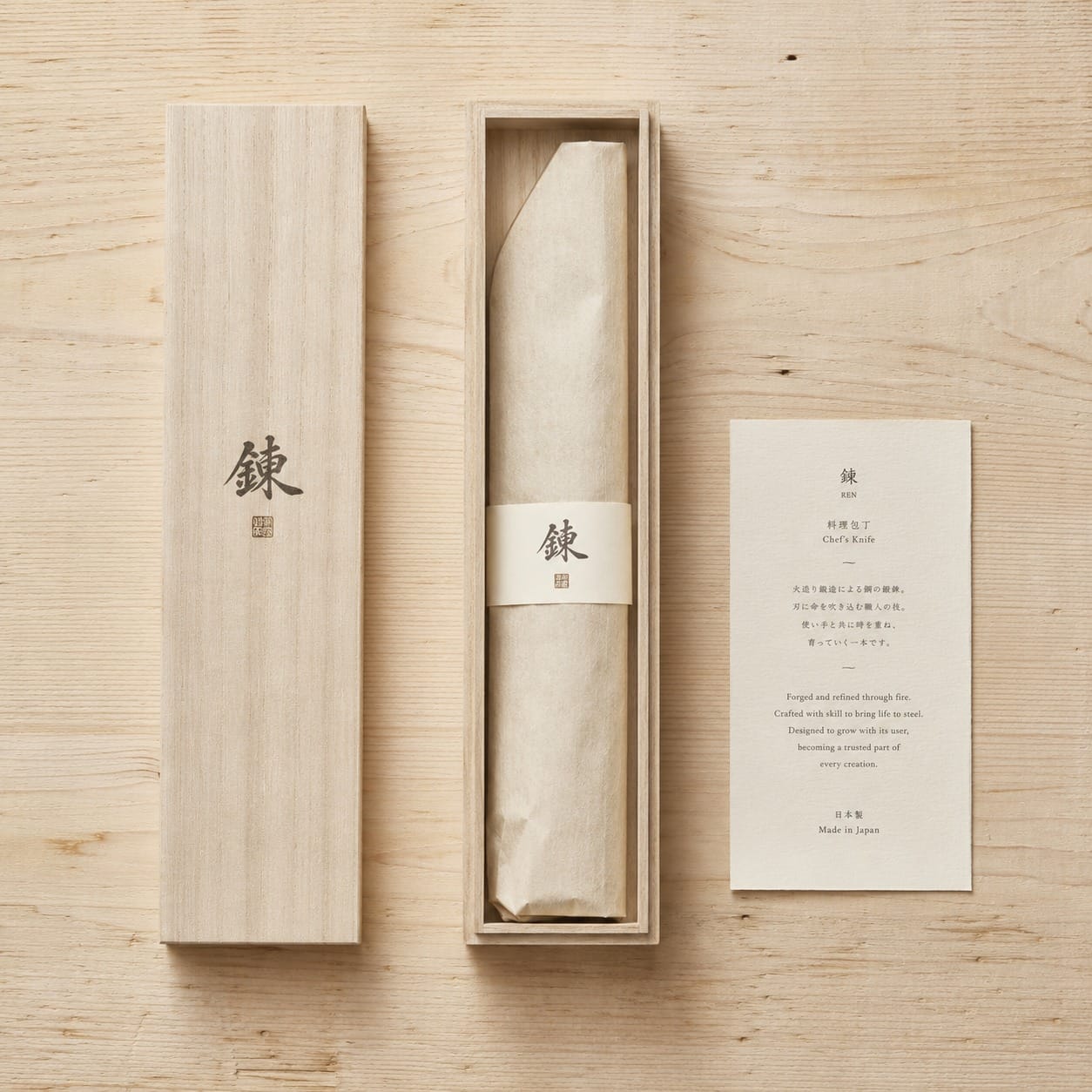 Flat lay of open paulownia wood box with washi-wrapped knife and letterpress maker card on hinoki surface