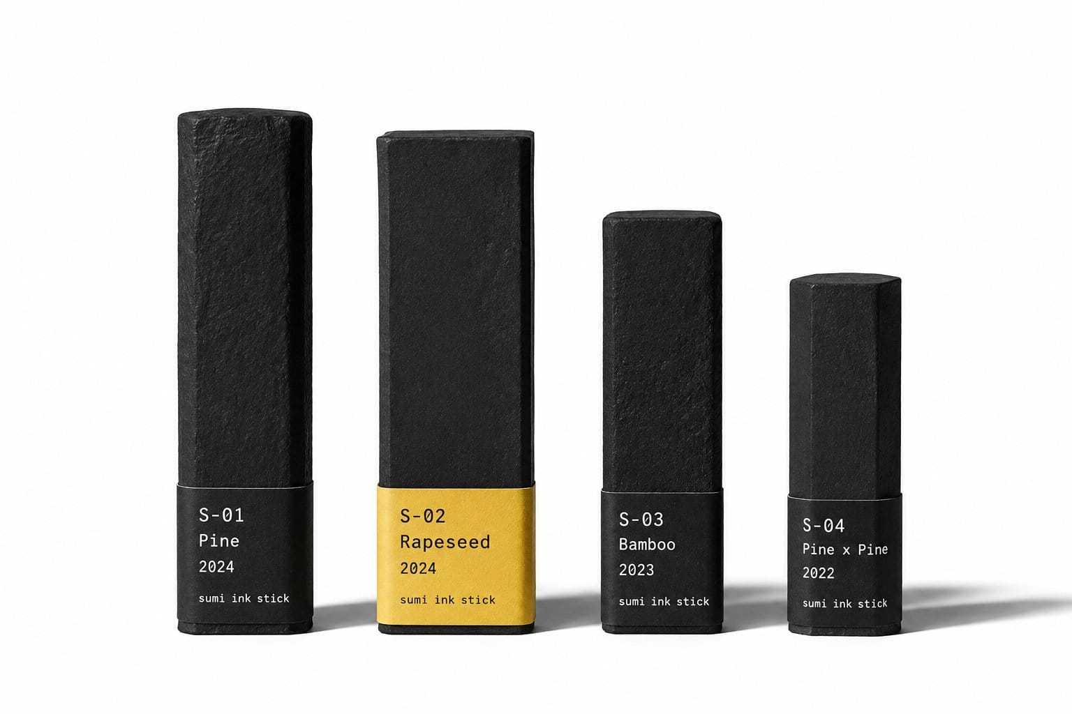 Four matte black sumi ink sticks lined up on a paper-white background, each with a letterpress catalog label band at the base, the S-02 Rapeseed stick wearing the saffron band
